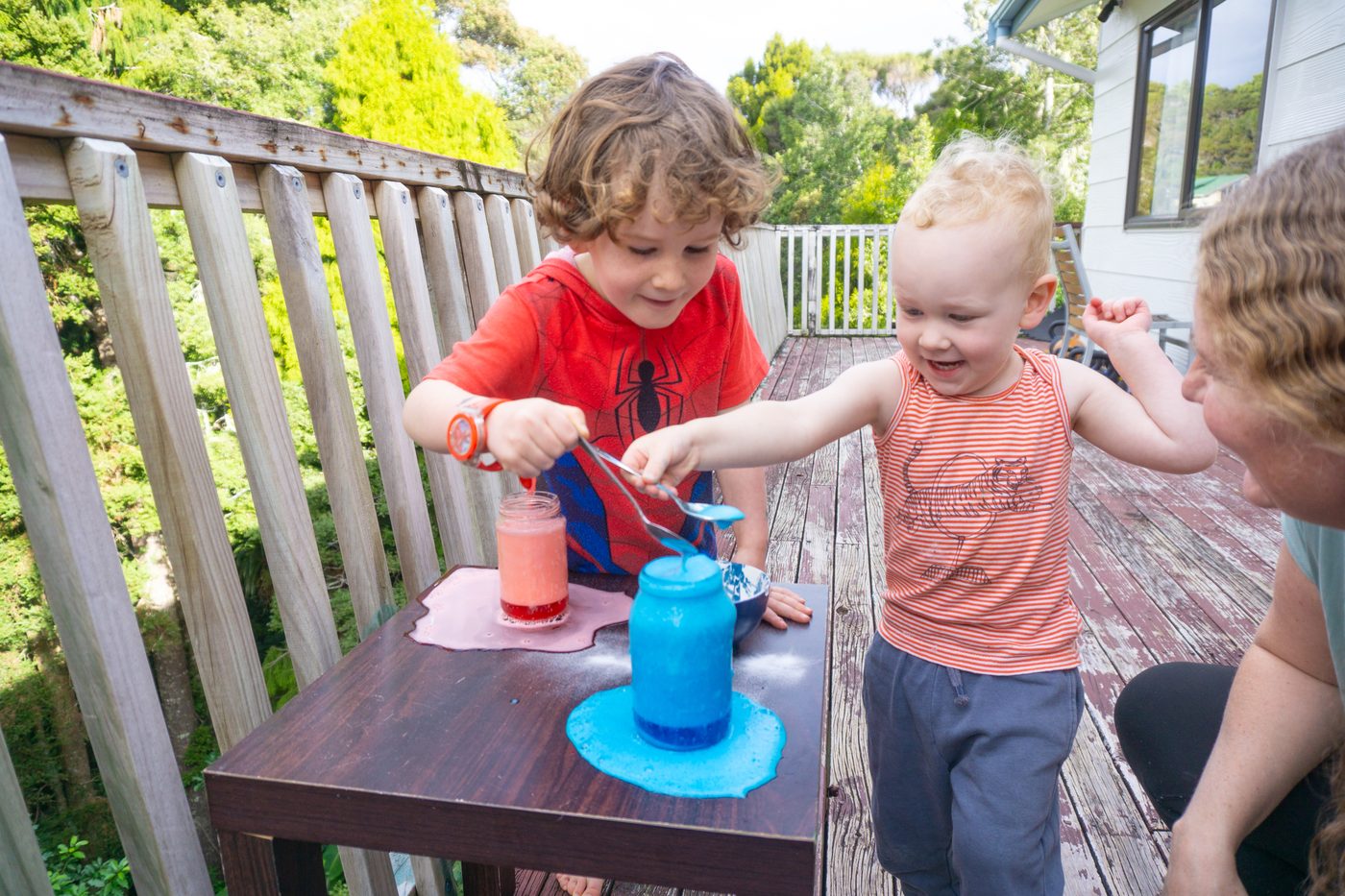 Two children on a deck watching red and blue jars fizz and bubble over